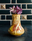 Sunstone Snowdrop vase with purple hellebore flowers on a dark slate surface against a Pewabic tiled wall.