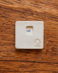 Back of a 3" x 3" tile with stamped-in notch for hanging. It is also stamped with the Pewabic logo, "Detroit", and specific Pewabic maker's mark. 