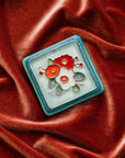 A Hand-Painted Three Flowers Tile in our "Poppy Palette" rests on a bed of rich, organge-pink velvet. 