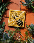 A glossy hand-painted Honeybee Tile in golden honey and black details surrounded by thistle. 
