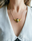 Necklace with a glossy, hand-painted bee pendant worn by a person wearing a dress with a large, white collar. 