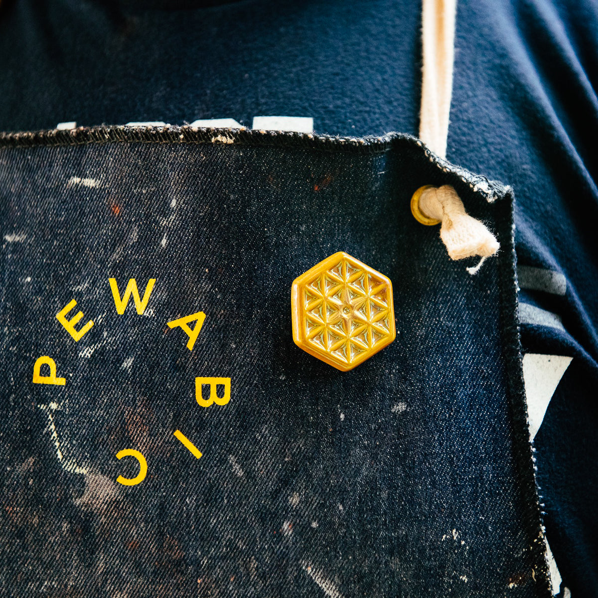 The small hexagonal Hex Pin features a line design of many interconnected triangles. The center has a tiny hexagon with a six-sided starburst emanating into the triangles. This pin features the  the gold metallic Blush Iridescent glaze.